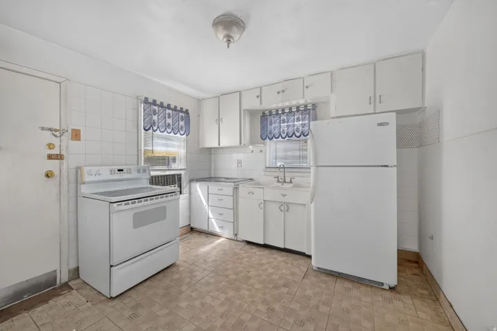 Kitchen featuring white cabinetry and appliances, tile flooring, and a window above the sink