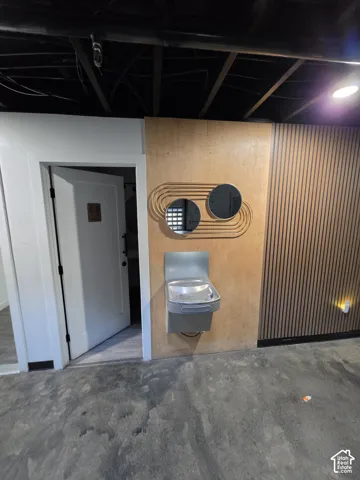 Exposed ceiling joists with black finish, concrete-finish flooring, wood wall paneling, and a built-in water fountain