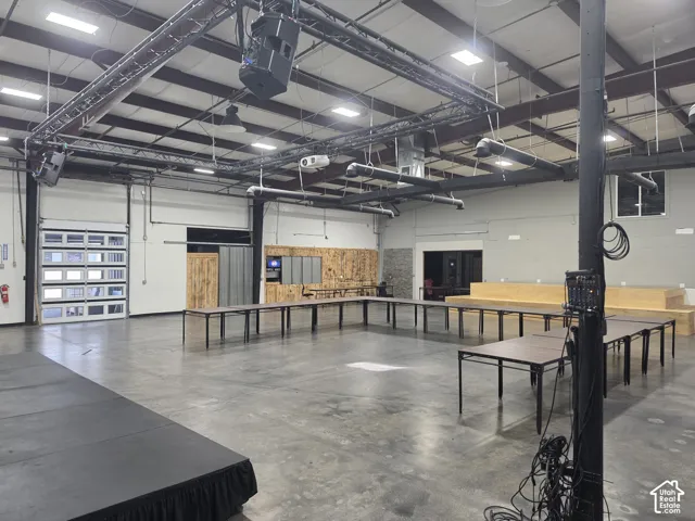 Expansive open space featuring high ceilings, exposed ductwork, a concrete floor, and a large roll-up glass garage door
