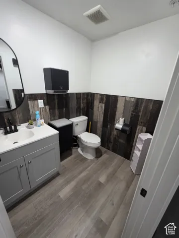 Modern vanity with a single basin sink and black faucet, wood-finish flooring, and dark wood-paneled accent wall