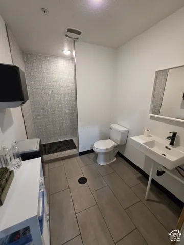 Walk-in shower with decorative tiled surround, wall-mounted sink, and plank-style floor tiles