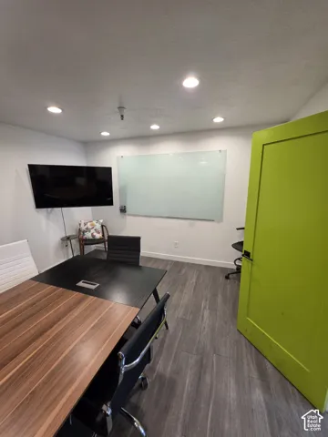 Recessed lighting, wood-finish plank flooring, wall-mounted television, white board, and solid core door