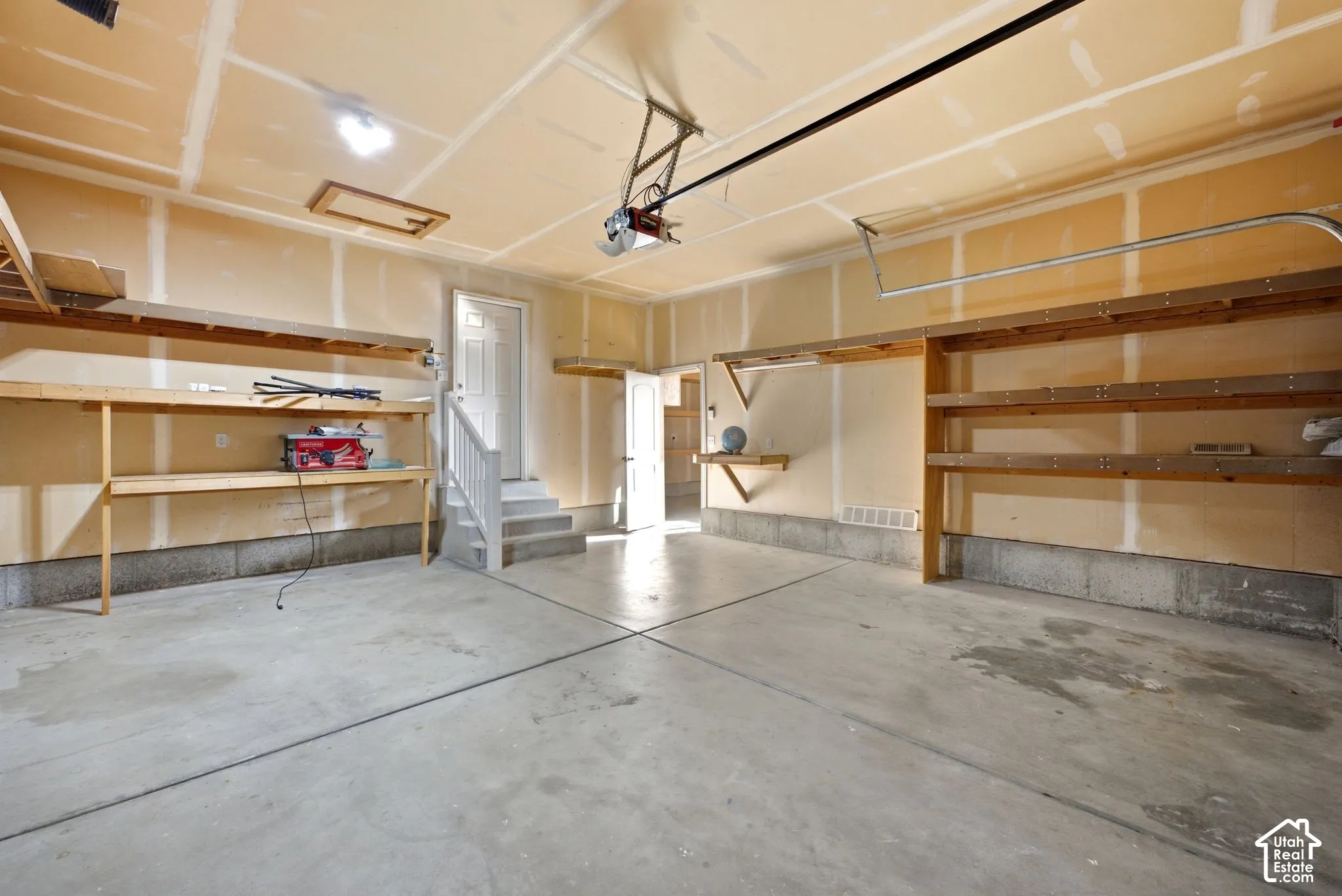 Concrete flooring, built-in shelving, white door, overhead lighting, and an automatic garage door opener
