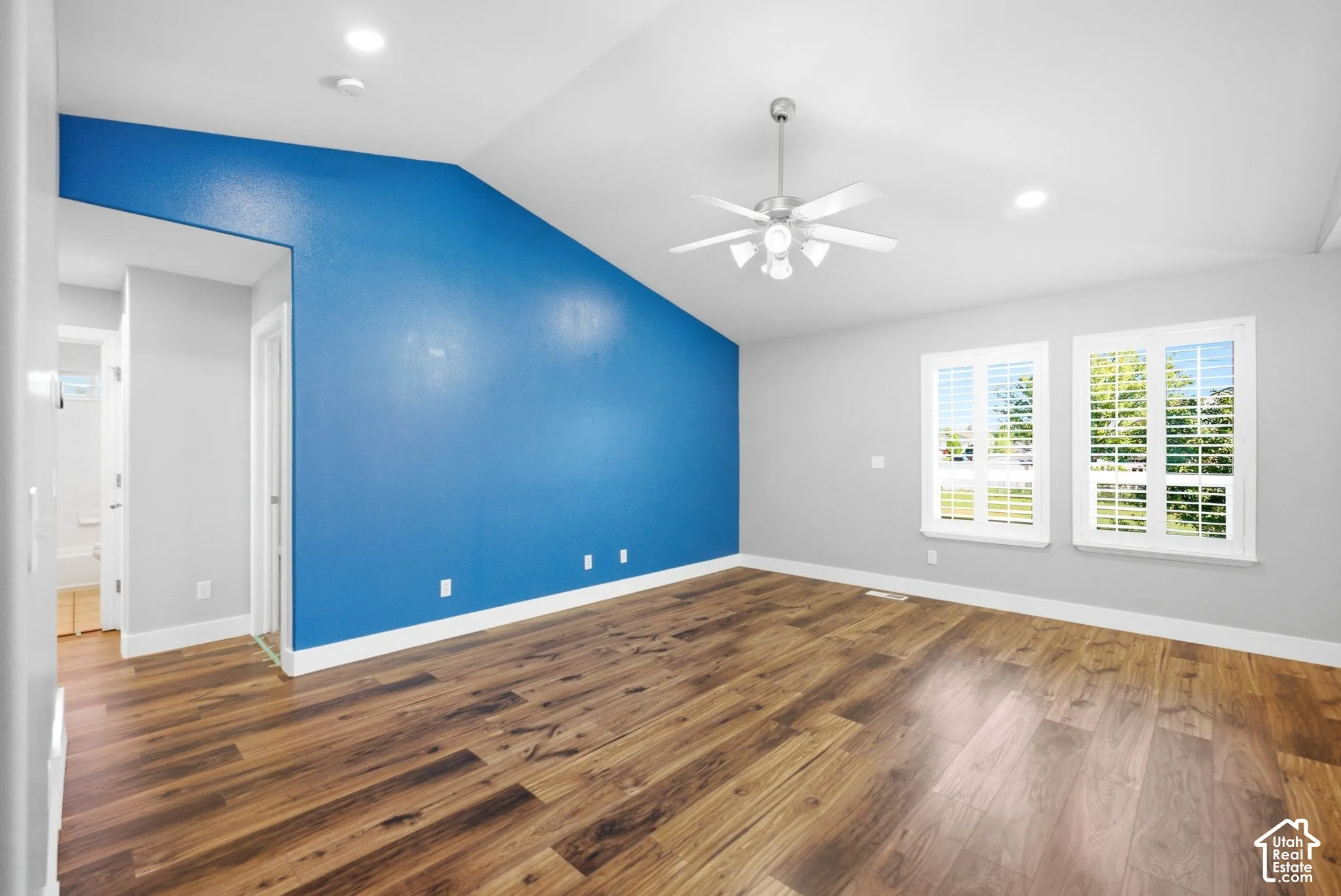 Vaulted ceiling with a ceiling fan, two windows with white plantation shutters, wood-finish flooring, recessed lighting, and a vibrant accent wall