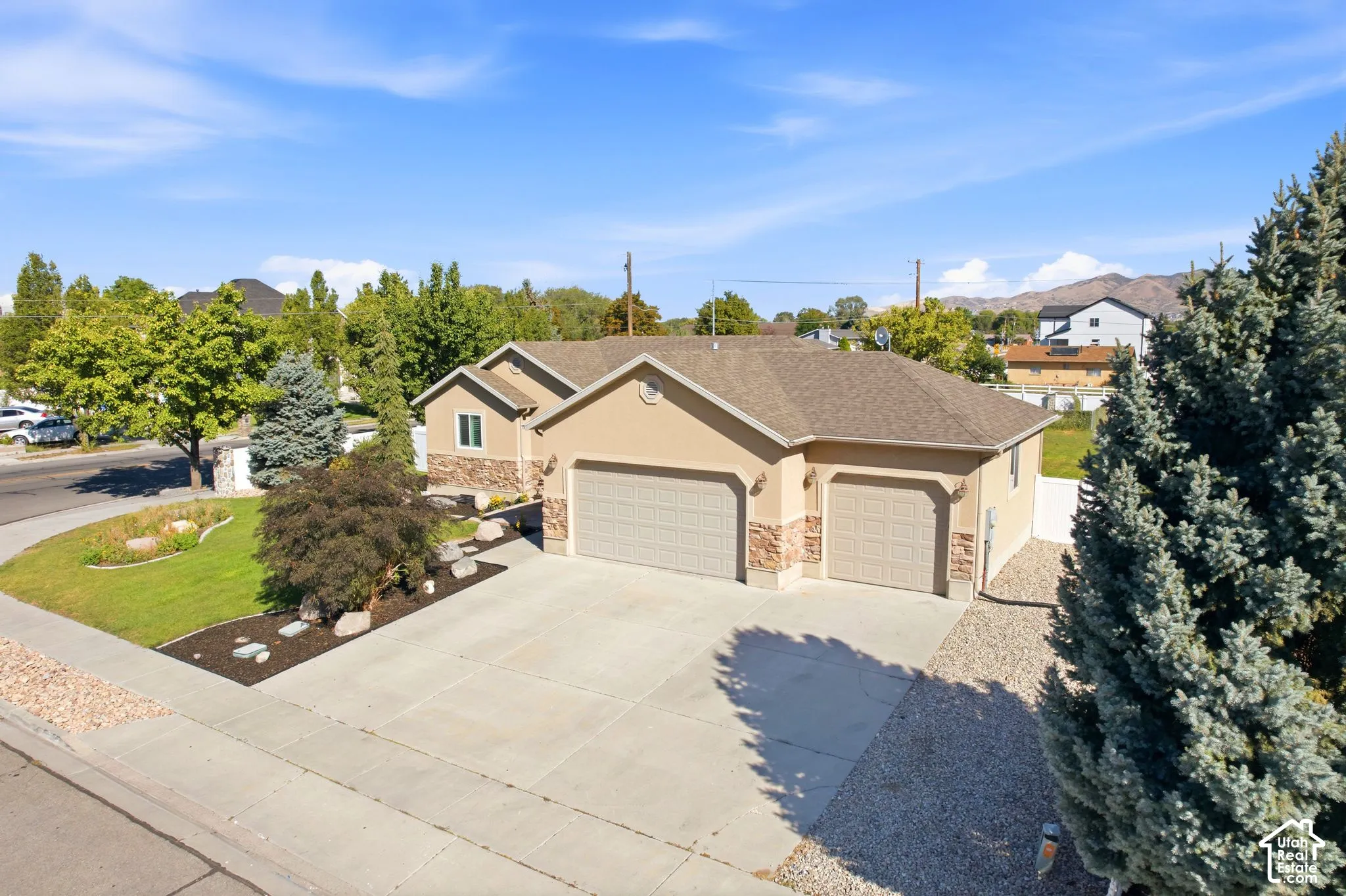 Stucco exterior with stone accents, attached two-car garage, concrete driveway, landscaped front yard with mature plantings, and a gravel side yard