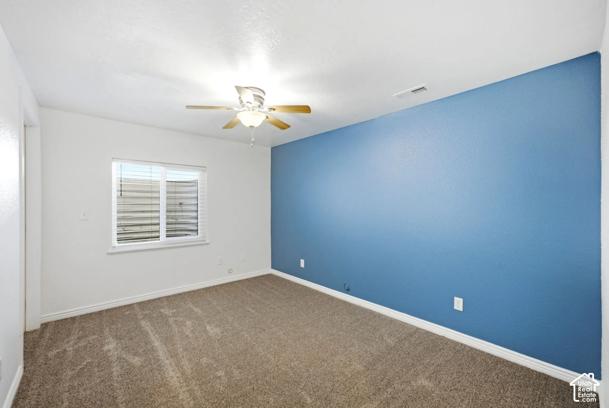 Carpeted flooring, a window with horizontal blinds, a ceiling fan with integrated lighting, and a contrasting accent wall