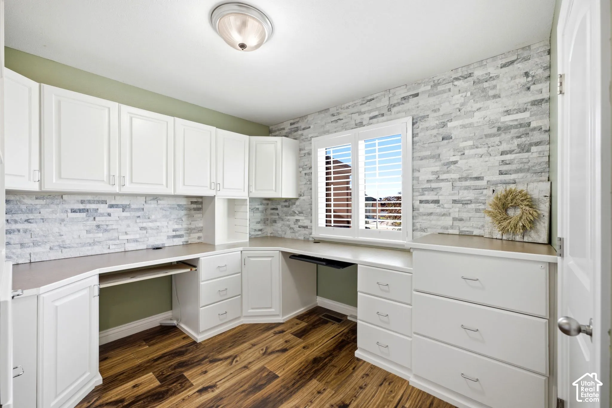 Built-in desk cabinetry with white shaker-style doors, wood-finish flooring, and a stacked stone accent wall