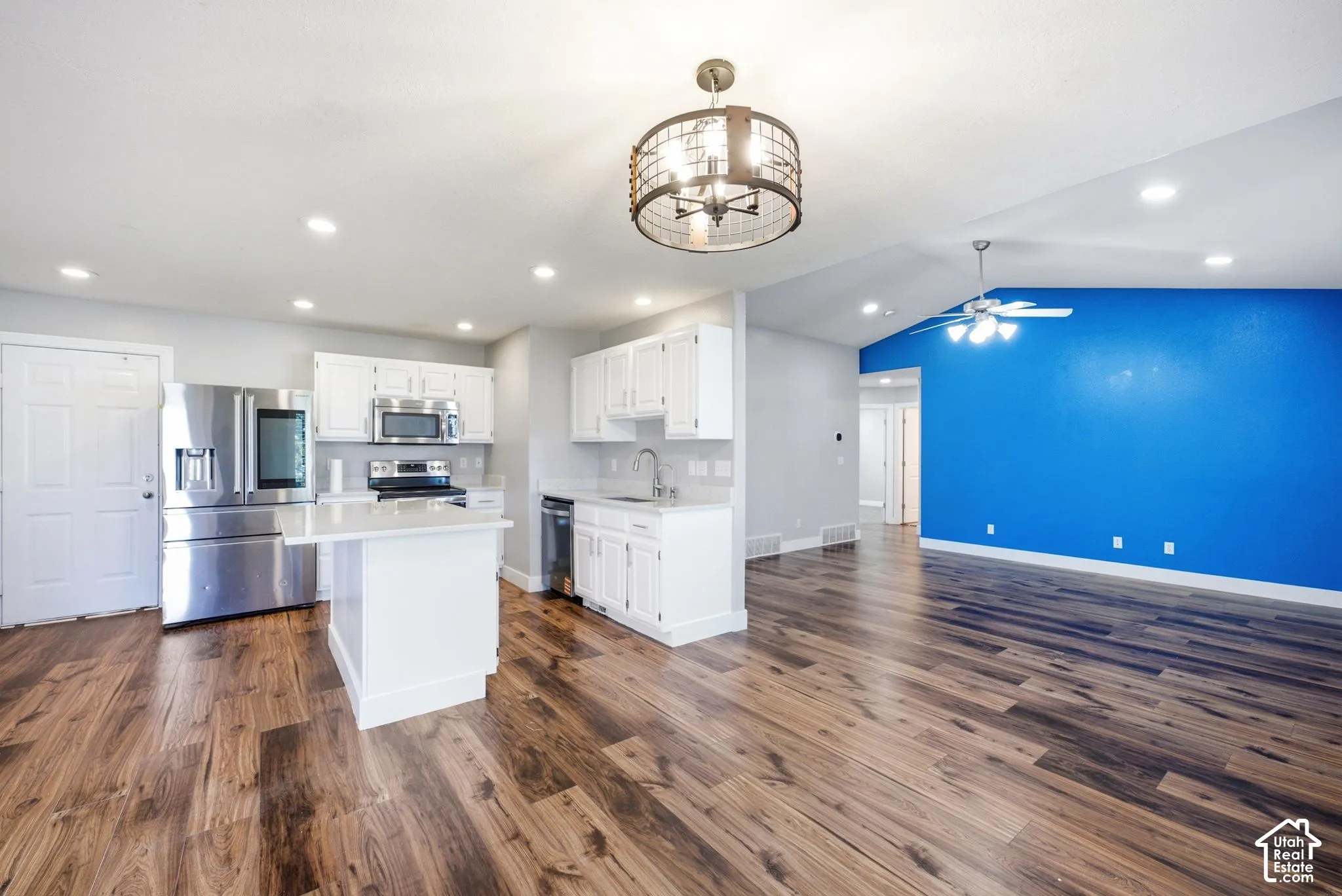 Open-concept kitchen and living area featuring wood-finish flooring, white cabinetry, stainless steel appliances, and vaulted ceilings