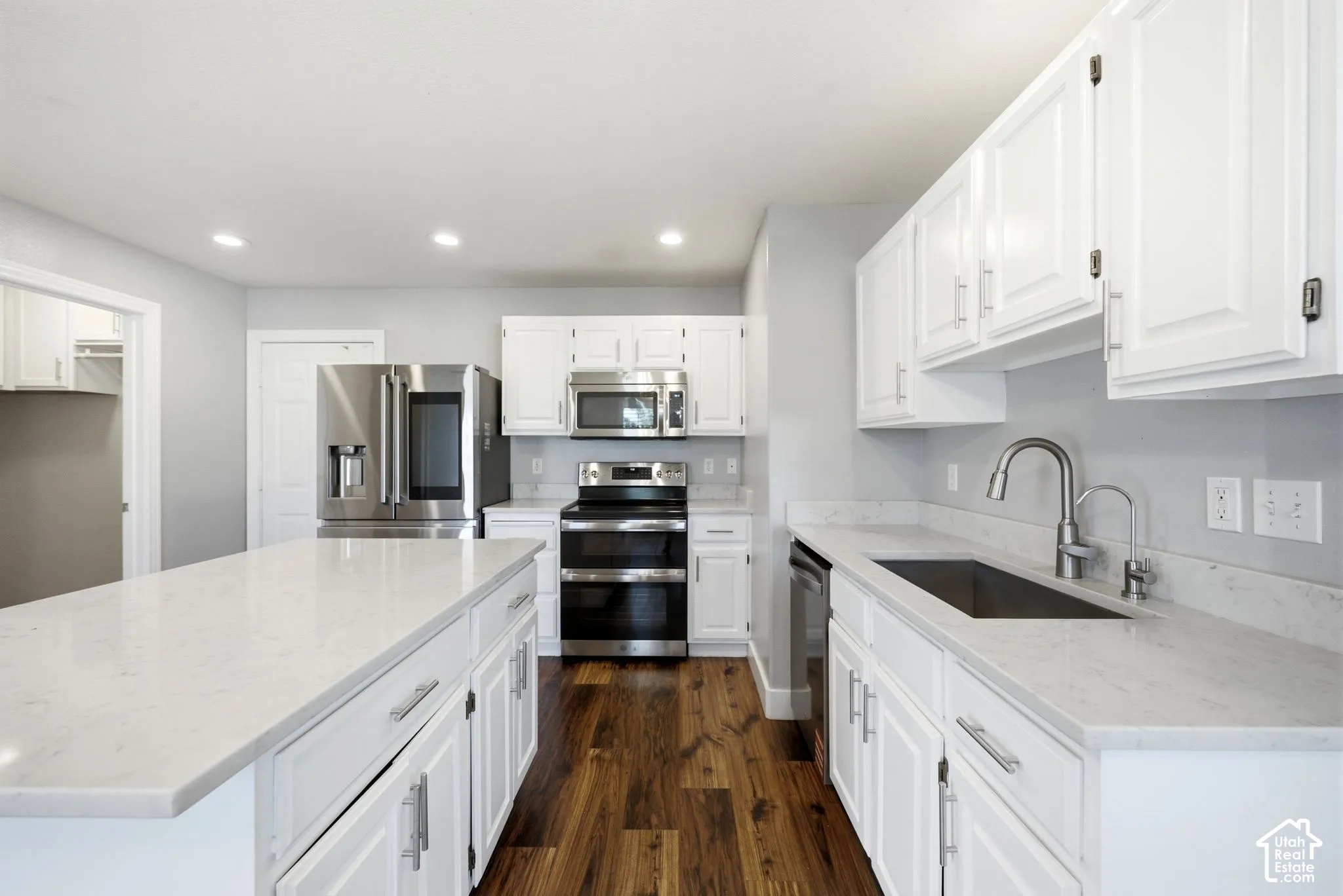 White shaker cabinetry with brushed nickel hardware, stainless steel appliances, solid surface countertops, a single basin sink with gooseneck faucet, and wood-finish flooring