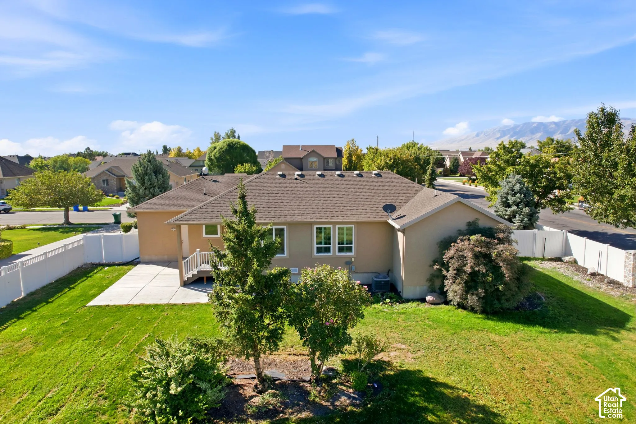Expansive backyard with a manicured lawn, concrete patio, white vinyl fencing, and mature trees