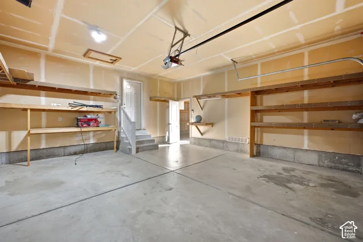 Concrete flooring, built-in shelving, white door, overhead lighting, and an automatic garage door opener