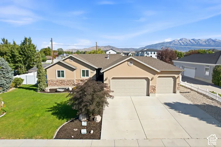Siding exterior with stone accents, attached two-car garage, concrete driveway, and landscaped front yard with mature plantings