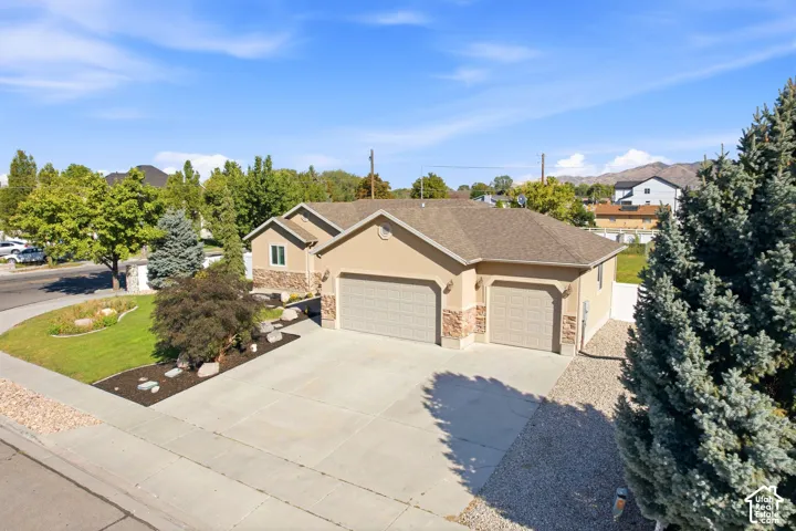 Stucco exterior with stone accents, attached two-car garage, concrete driveway, landscaped front yard with mature plantings, and a gravel side yard