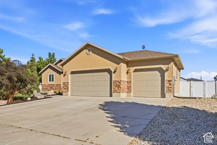 Stucco exterior with stone accents, concrete driveway, two garage doors, and a partial white privacy fence