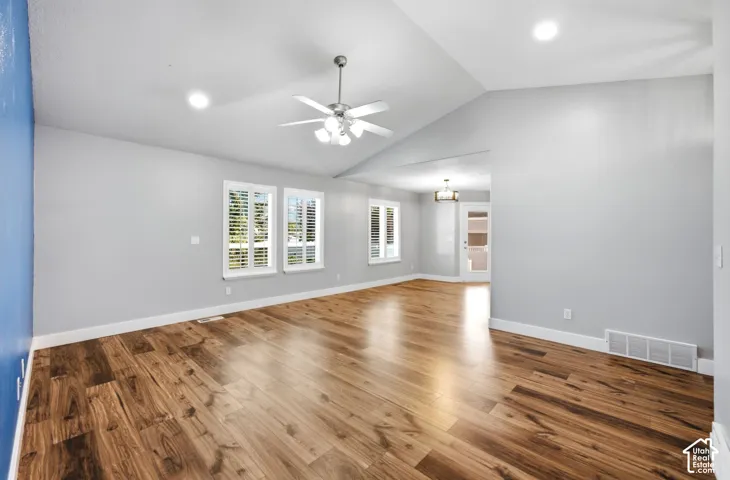 Vaulted ceilings with recessed lighting, wood-finish flooring, two windows with louvered shutters, and a ceiling fan with integrated lighting