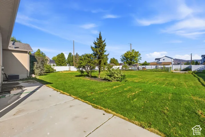 Expansive green lawn with mature landscaping, fenced perimeter, and concrete patio