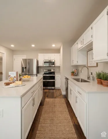 Kitchen featuring white shaker-style cabinetry, stainless steel appliances, light-toned countertops, wood-finish flooring, and recessed lighting
