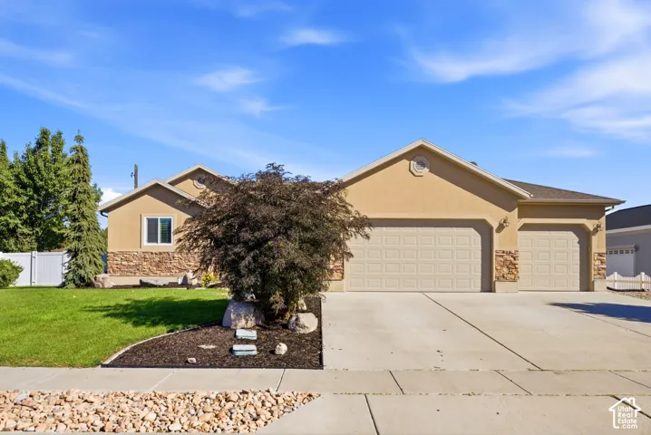 Stucco exterior with stone accents, attached two-car garage, concrete driveway, front lawn, and landscaped garden bed