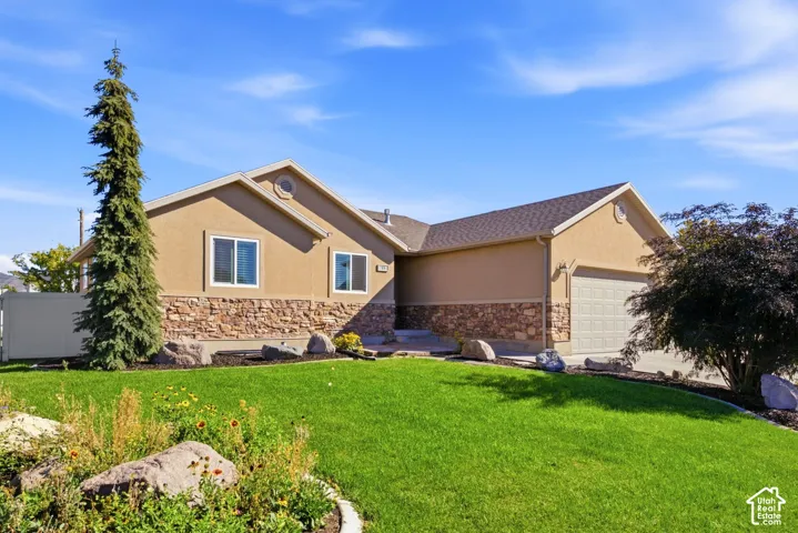 Stucco exterior with stone accent, attached garage, sloped roofline, and front landscaping
