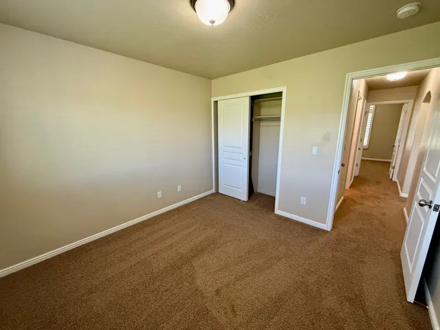 Bedroom 3- Neutral tone wall paint, brown carpet flooring, flush mount ceiling light, sliding closet doors, and white trim