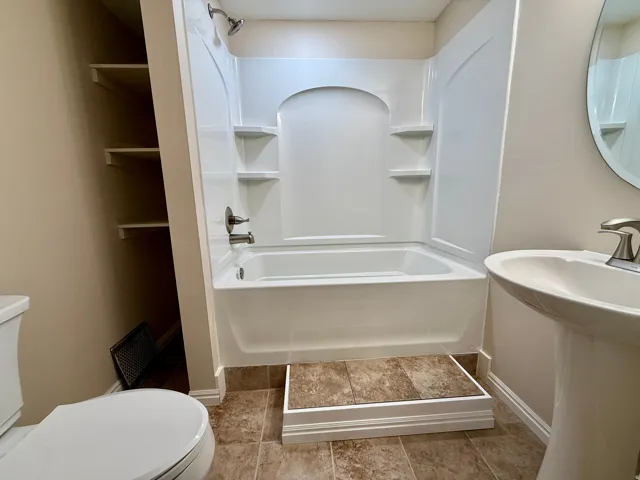 Bathroom 3- White acrylic bathtub with integrated shelving, brushed nickel fixtures, pedestal sink, and tiled flooring