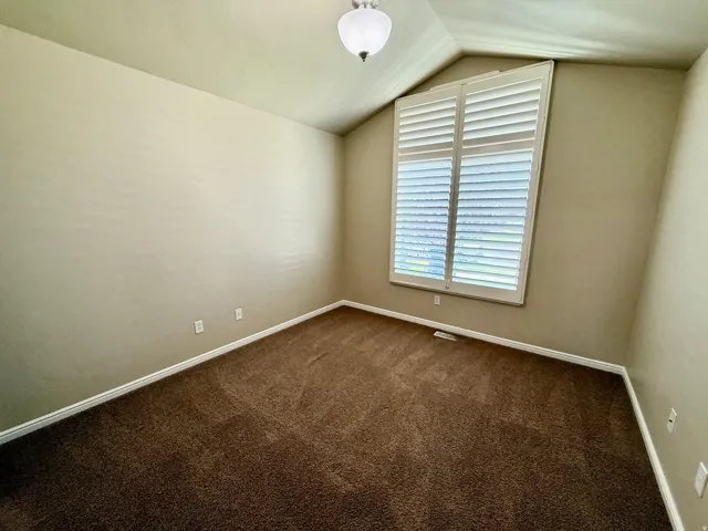 Bedroom 2- Vaulted ceiling, white plantation shutters, neutral wall color, and brown carpet