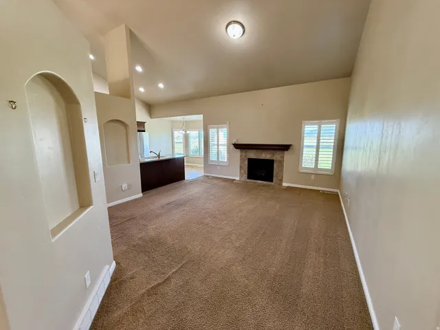 Vaulted ceiling with recessed lighting, stone-clad fireplace with wood mantel, built-in wall niches, and shutters on windows