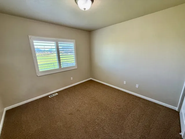 Bedroom 3- Neutral wall tones, brown carpet, and a window featuring white plantation shutters