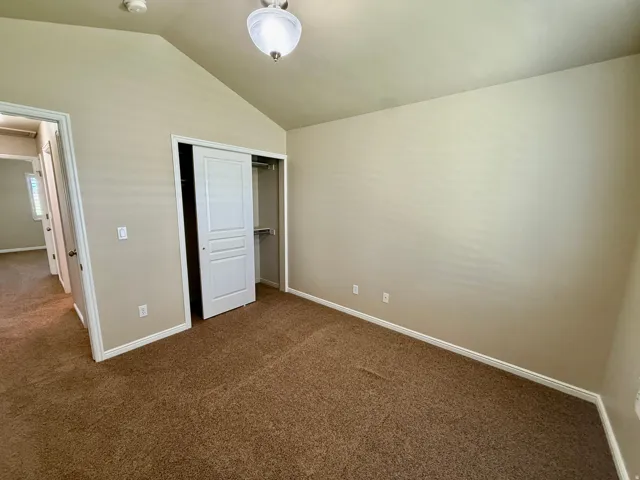 Bedroom 2- Vaulted ceiling with a flush-mount light fixture, neutral wall paint, brown carpet flooring, and a sliding closet door