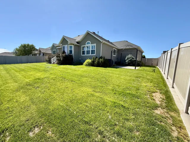 Expansive lawn, privacy fencing, stucco exterior, multiple large windows, and a paved patio area.