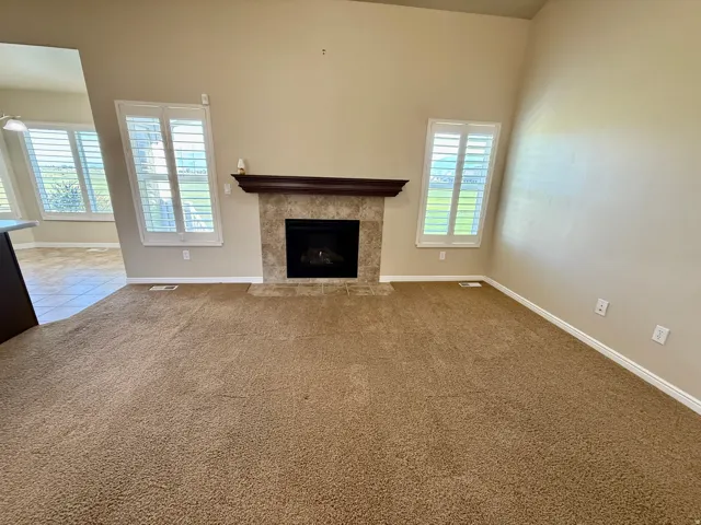 Vaulted ceilings, carpeted flooring, fireplace with stone surround, wood mantel, and plantation shutters