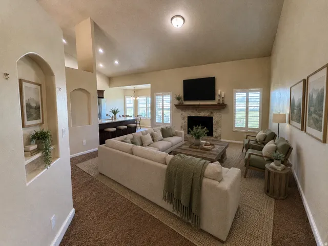 Vaulted ceiling with recessed lighting, stone-clad fireplace with wood mantel, built-in wall niches, and shutters on windows