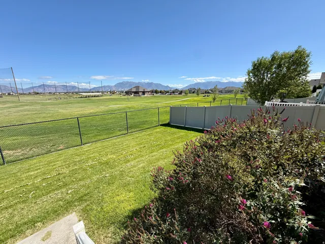 Cranefield Golf Course views- Expansive green space bordered by a chain-link fence,  Purple butterfly shrubs, and distant mountains
