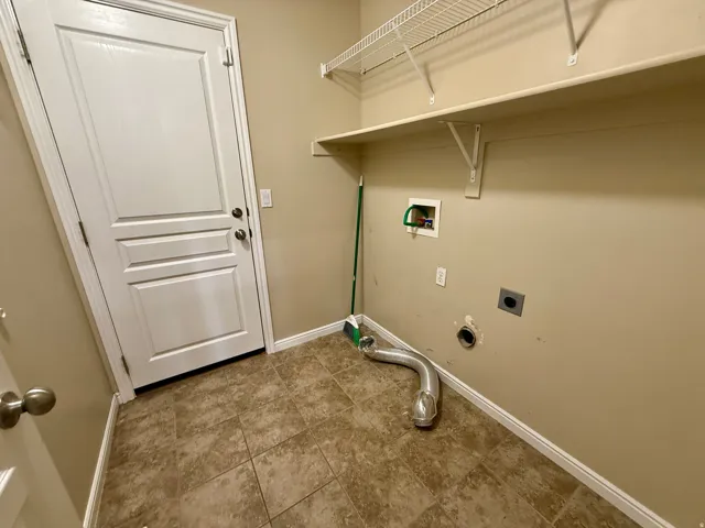 Laundry room- Tile flooring, white paneled door, built-in shelving, and utility hookups