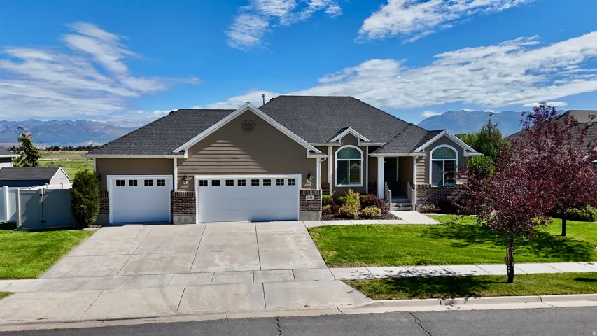 Single-story residence featuring a three-car garage, manicured front lawn, and mature landscaping