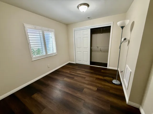 Bedroom 5, Wood-finish LVP flooring, white plantation shutters, neutral painted walls, recessed ceiling light, and a sliding closet door