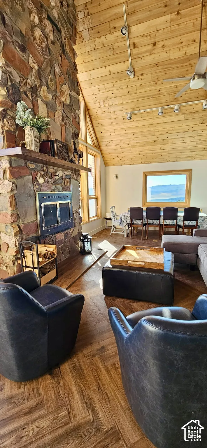 Vaulted wood-finish ceiling, stone fireplace with wood mantel, wood-finish flooring in a herringbone pattern, and large windows with natural wood frames
