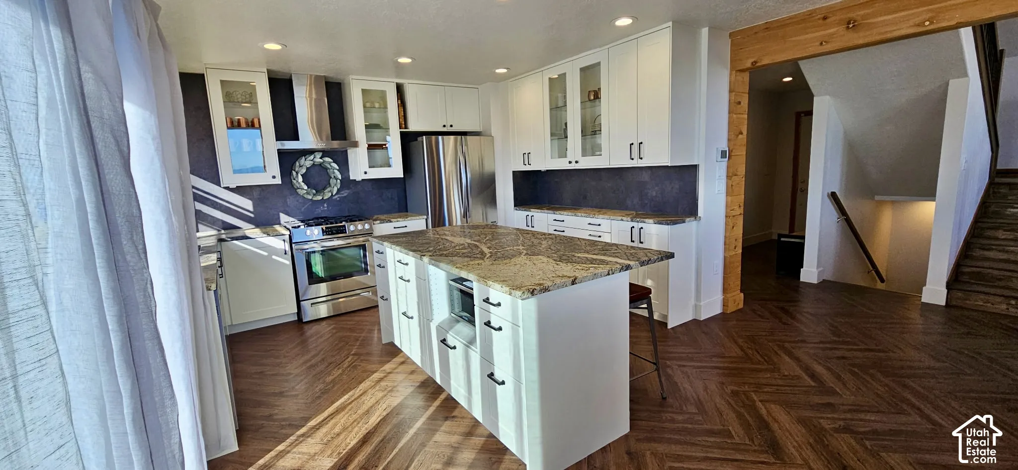 Kitchen featuring white cabinetry, stainless steel appliances, a large center island with a stone countertop, and wood-finish flooring with a chevron pattern