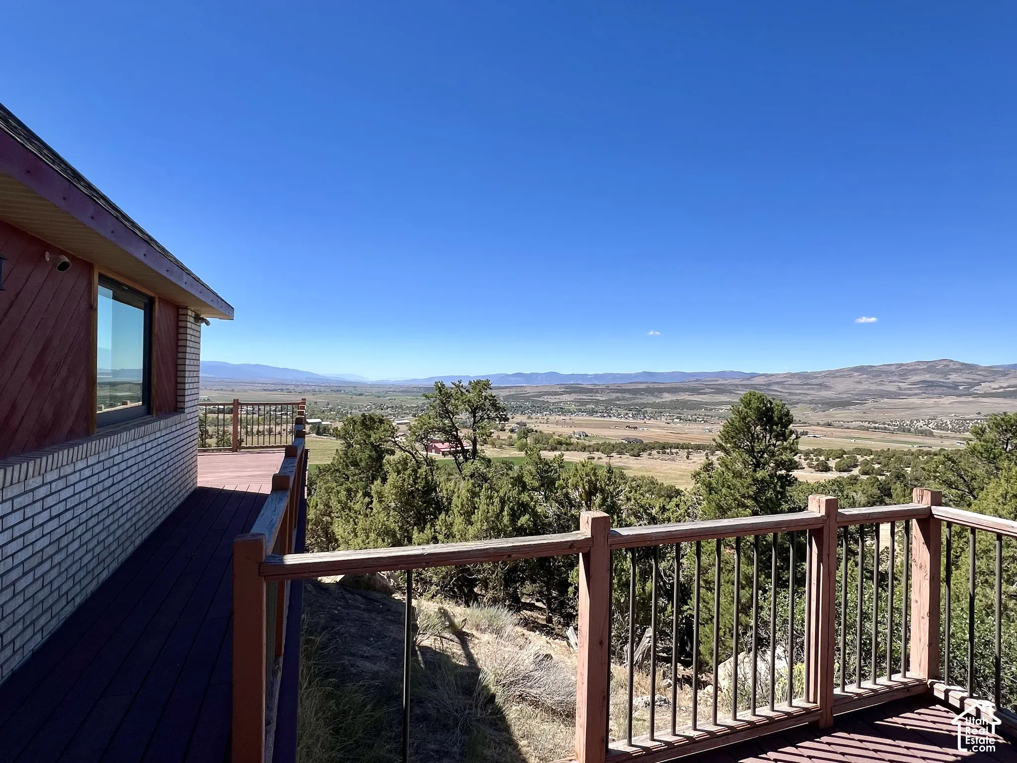 Expansive outdoor deck with wood-finish flooring and metal railings, overlooking a valley and distant mountains