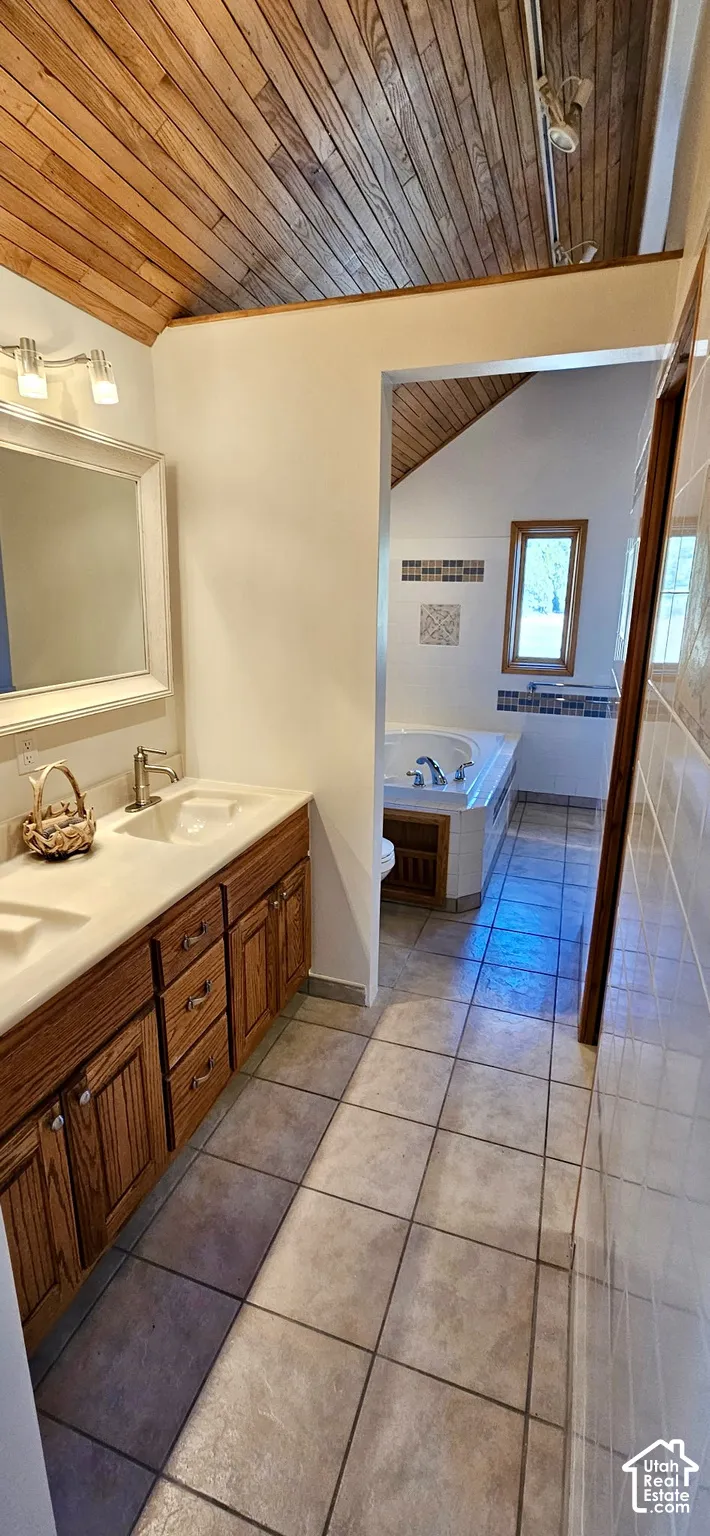 Bathroom featuring a wood-panel vaulted ceiling, a double vanity with wood cabinetry, and a built-in jetted tub