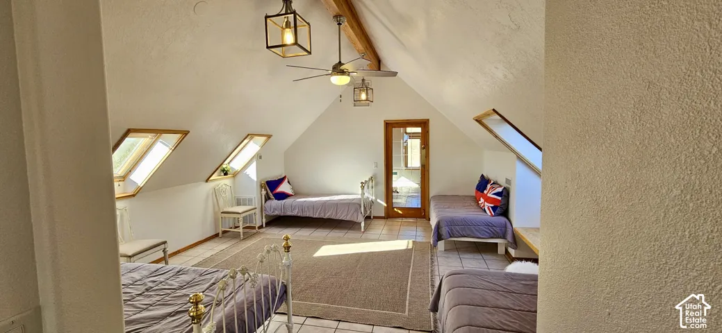 Angled ceilings with exposed wood beams, multiple skylights, ceiling fan, and tiled flooring