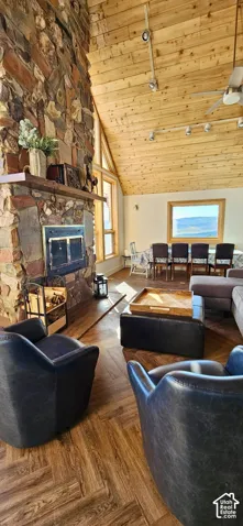 Vaulted wood-finish ceiling, stone fireplace with wood mantel, wood-finish flooring in a herringbone pattern, and large windows with natural wood frames
