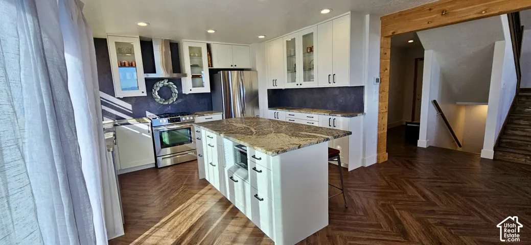 Kitchen featuring white cabinetry, stainless steel appliances, a large center island with a stone countertop, and wood-finish flooring with a chevron pattern
