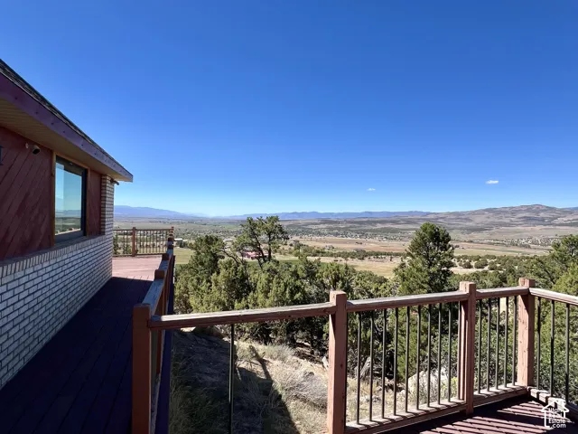 Expansive outdoor deck with wood-finish flooring and metal railings, overlooking a valley and distant mountains