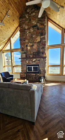 Vaulted wood-finish ceilings, an expansive stone fireplace, large windows with natural wood frames, and wood-finish flooring in a herringbone pattern
