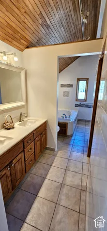 Bathroom featuring a wood-panel vaulted ceiling, a double vanity with wood cabinetry, and a built-in jetted tub