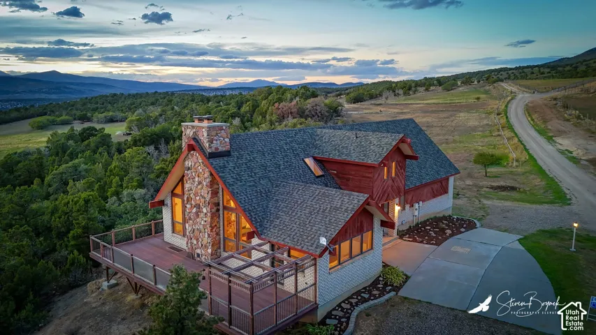 Stone and wood exterior with a large wrap-around deck, covered driveway, and expansive natural scenery