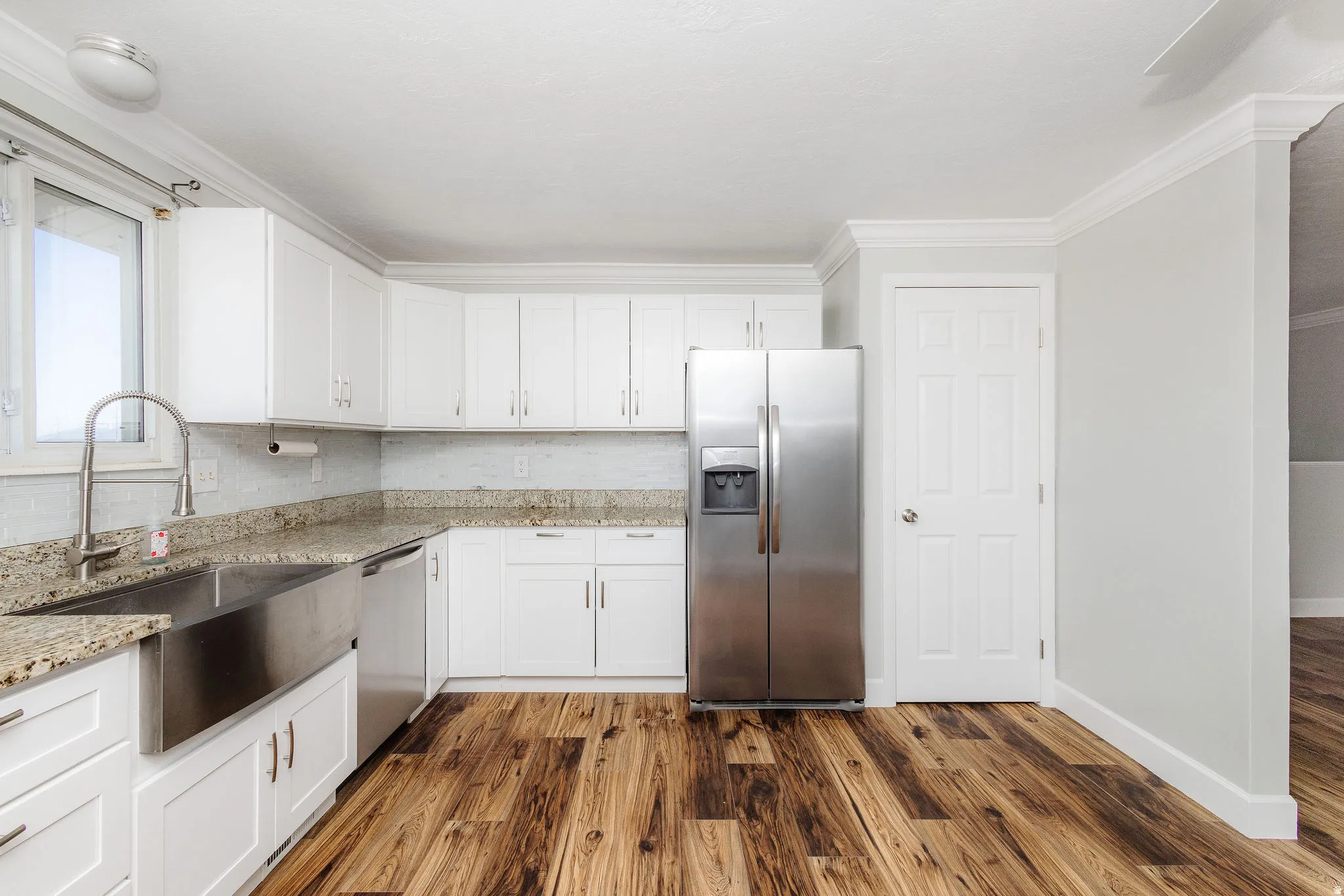 Kitchen featuring white cabinetry, granite countertops, a stainless steel apron sink, a stainless steel refrigerator, and wood-finish flooring