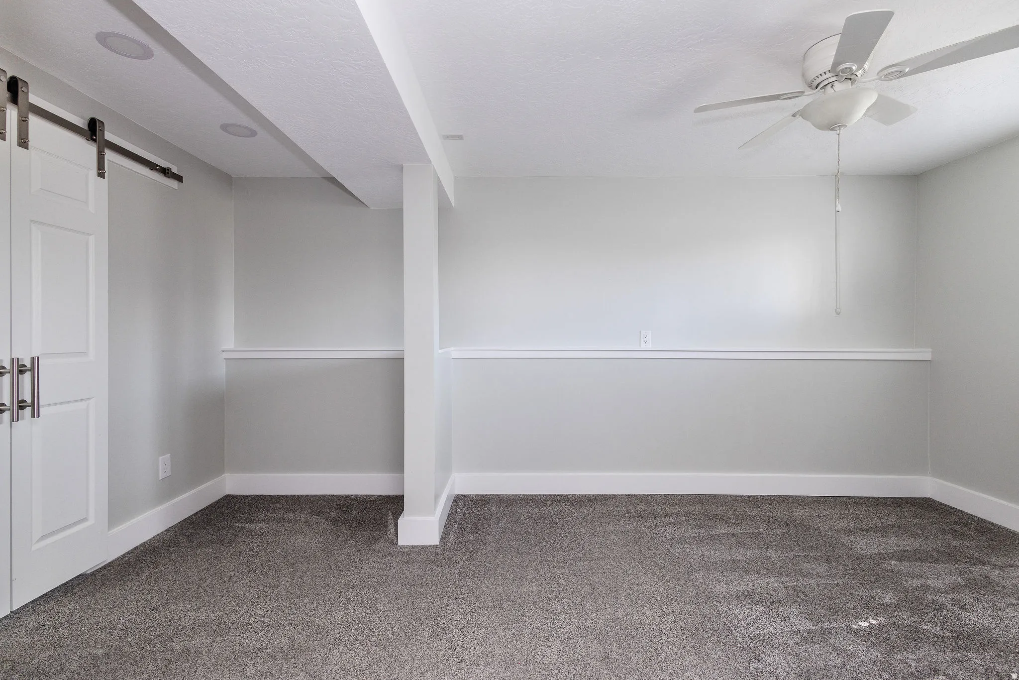 Spacious room featuring gray textured carpeting, white chair rail molding, and a ceiling fan