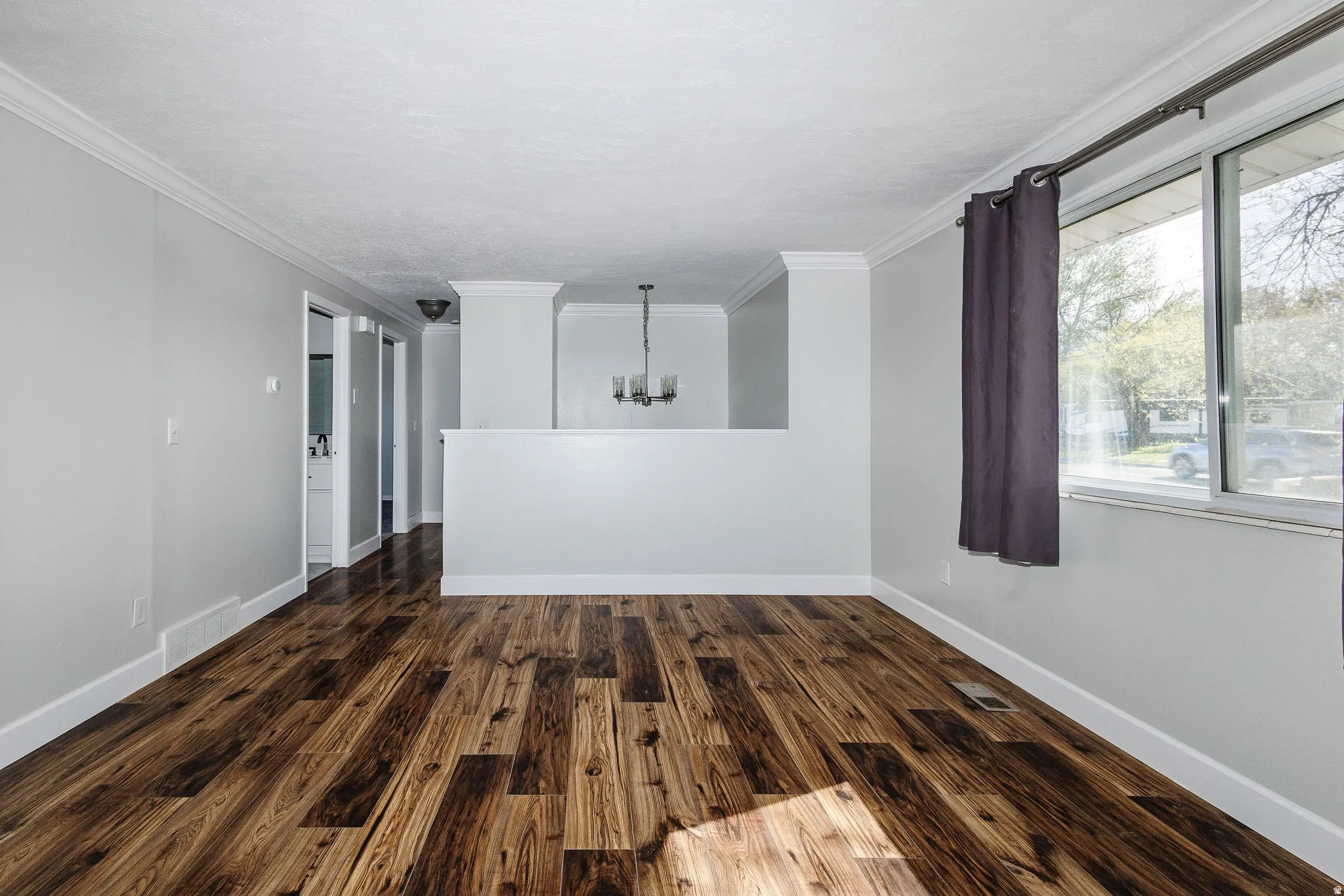 Wood-finish flooring, white crown molding, white baseboards, and a contemporary chandelier
